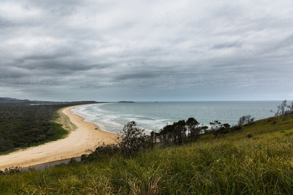 Looking down at beach from up high on hill sand waves and clouds - Australian Stock Image