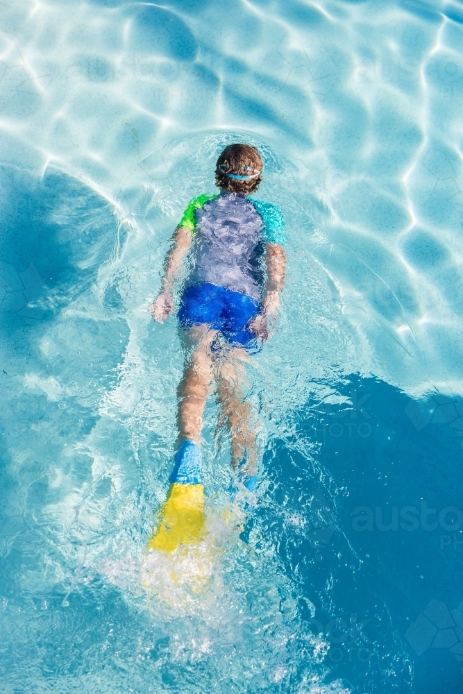 Looking down at boy wearing flippers and goggles gliding in swimming pool - Australian Stock Image