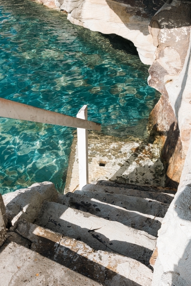 looking down at natural stone steps leading into the aqua ocean - Australian Stock Image