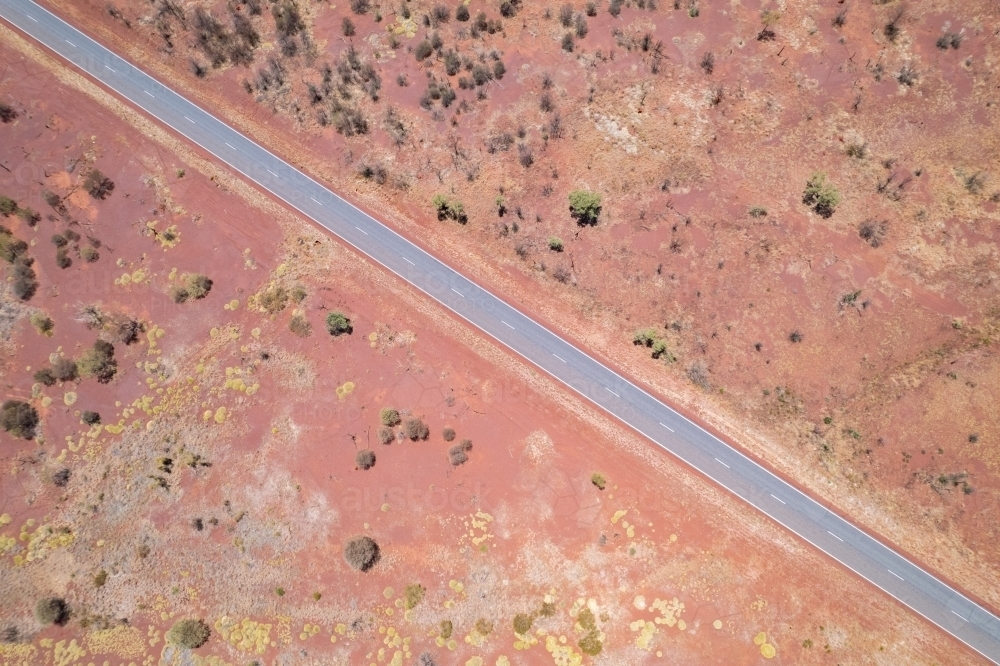 Looking down at the diagonal asphalt road with the red dirt and bushes on both sides of t : Austockphoto Looking down at the diagonal asphalt road with the red dirt and bushes on both sides of t - Australian Stock Image