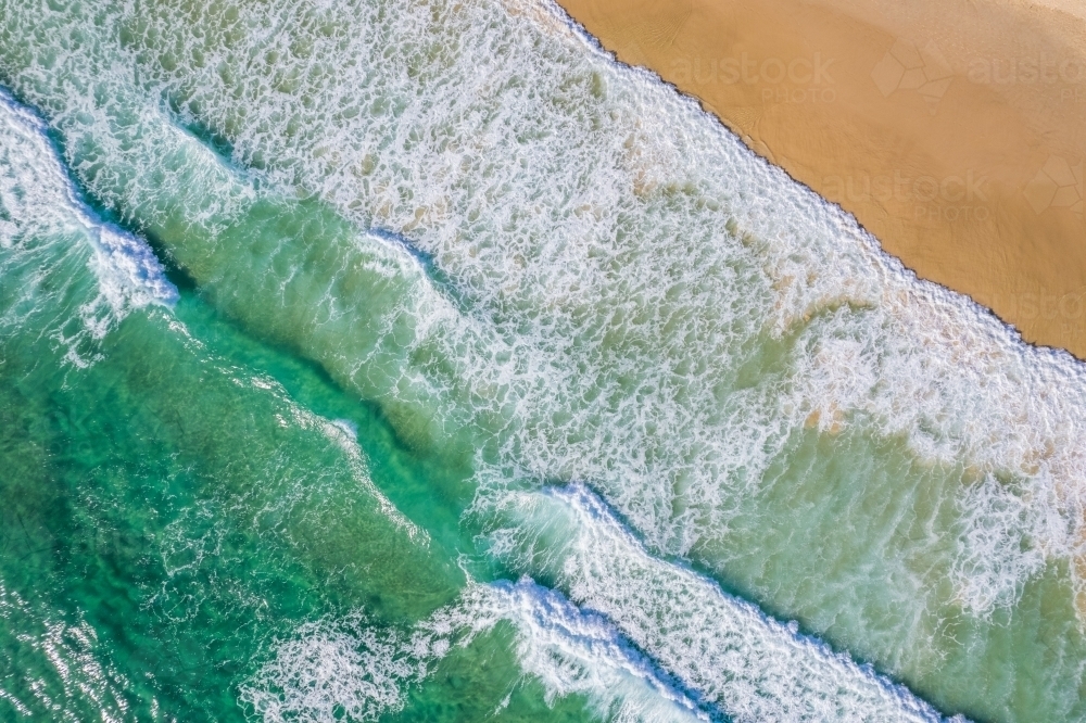 Looking down at the surf coming onto the sand at an isolated beach - Australian Stock Image