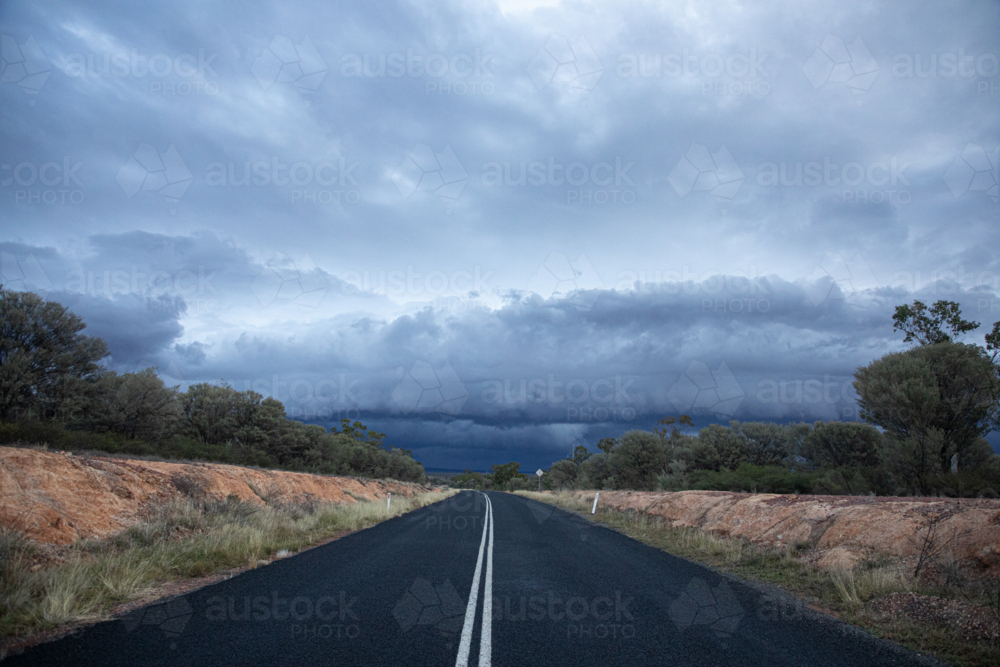 Looking down double white lines on a bitumen road towards a shelf cloud. - Australian Stock Image