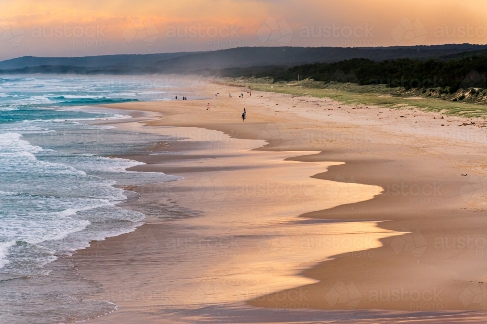 Looking down on a beautiful sunset lit beach with people in the distance. - Australian Stock Image
