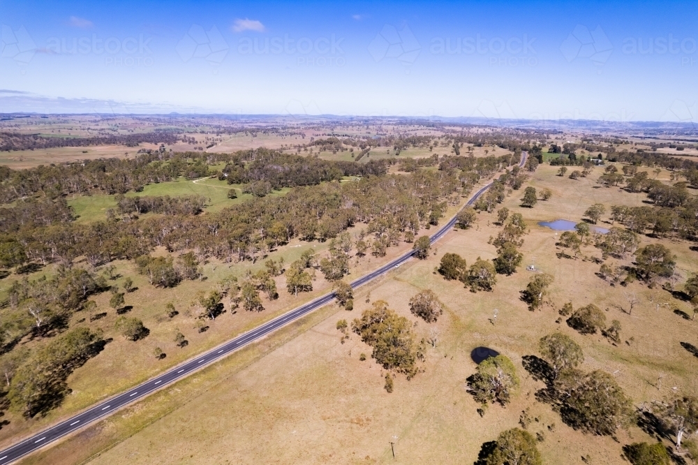 Looking down on a brown rural countryside with a single asphalt highway going off in the distance - Australian Stock Image