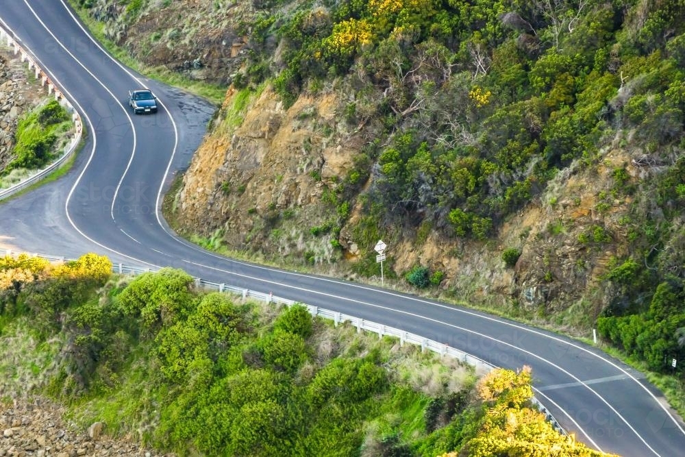Looking down on a  car driving on a winding road in the hills - Australian Stock Image