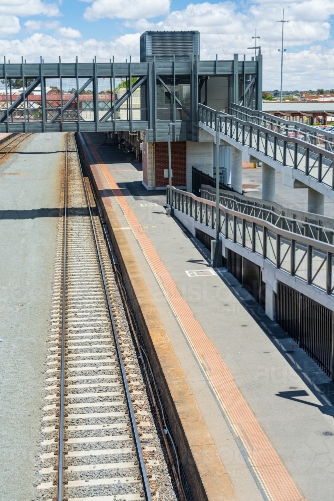 Looking down on a deserted railway platform with access ramps and an overhead walkway - Australian Stock Image