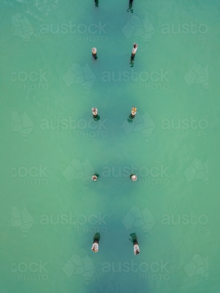 Looking down on a row of old jetty pylons in turquoise water - Australian Stock Image
