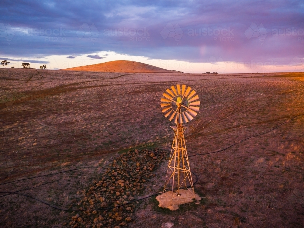 Looking down on a windmill in a dry paddock with a mountain on the horizon - Australian Stock Image