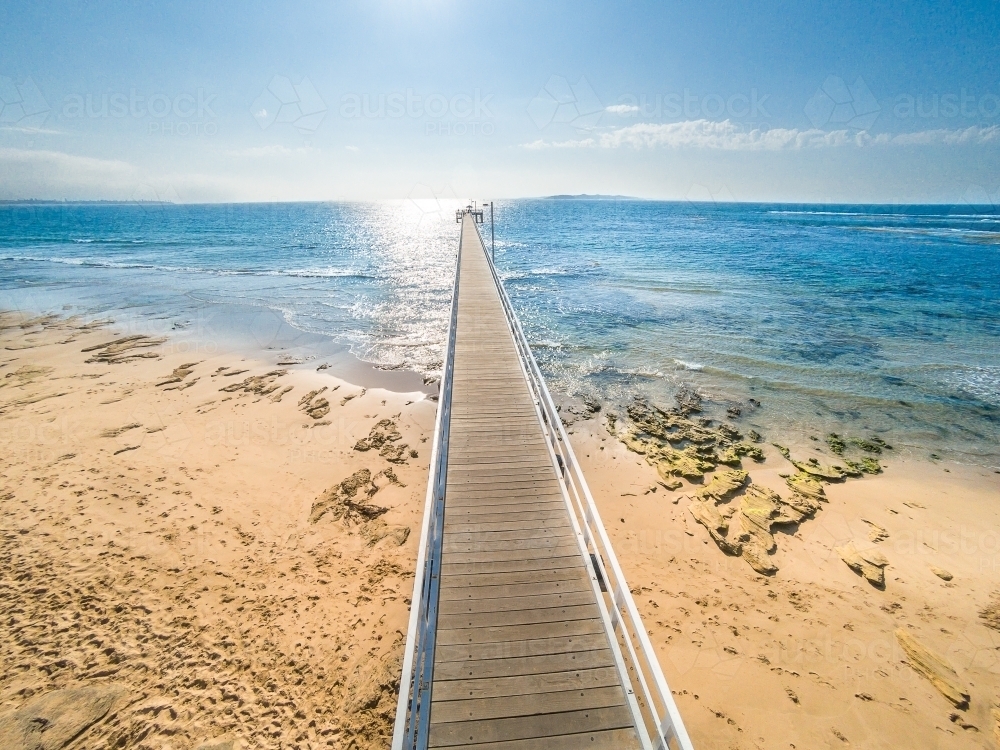 Looking down on a wooden jetty jutting out into the blue ocean on a sunny day - Australian Stock Image