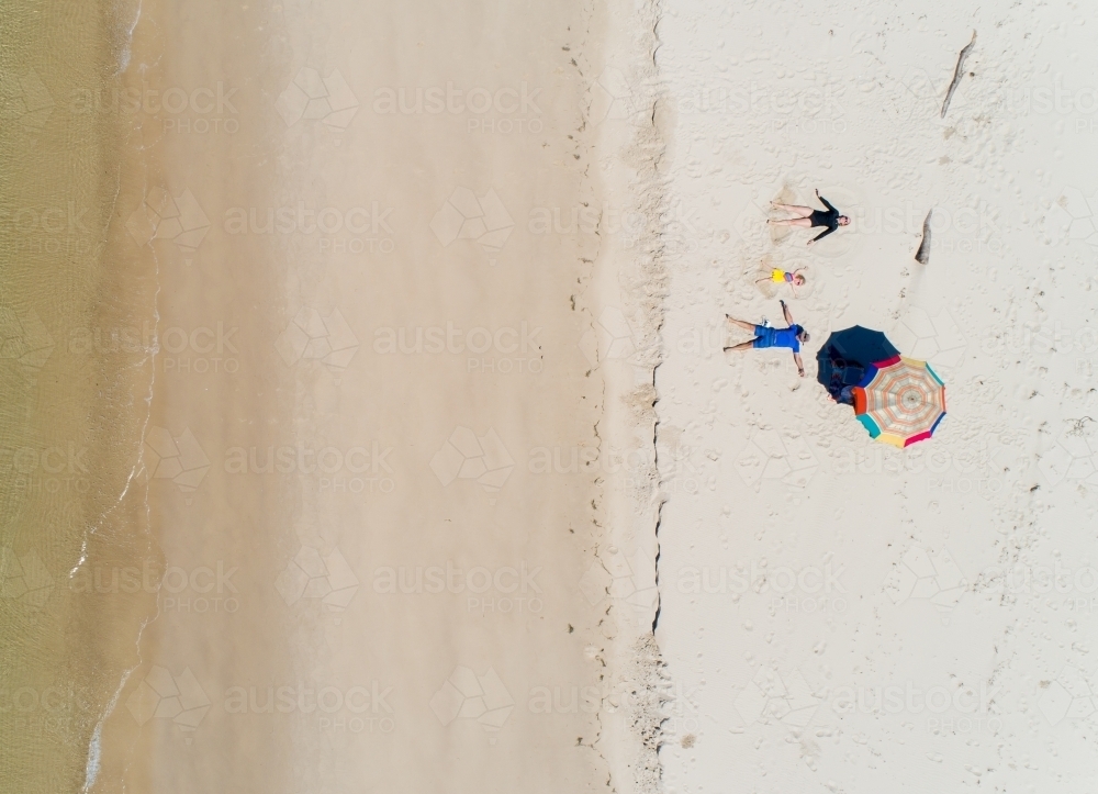 Looking down on family making sand angels on a beach. - Australian Stock Image