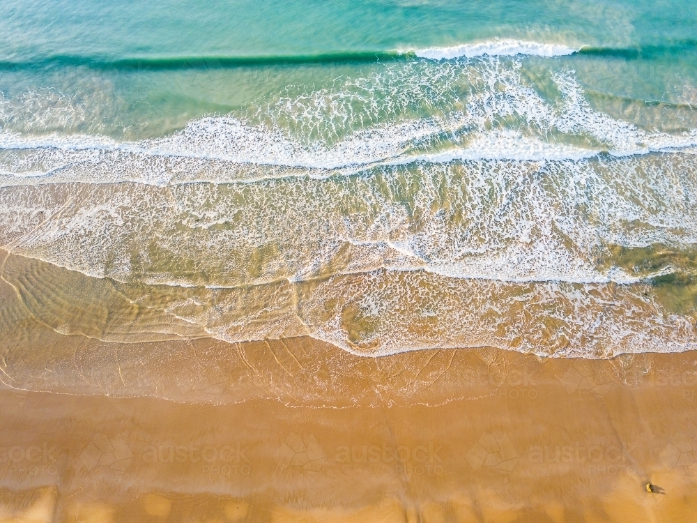 Looking down on gentle waves breaking on a sandy beach - Australian Stock Image