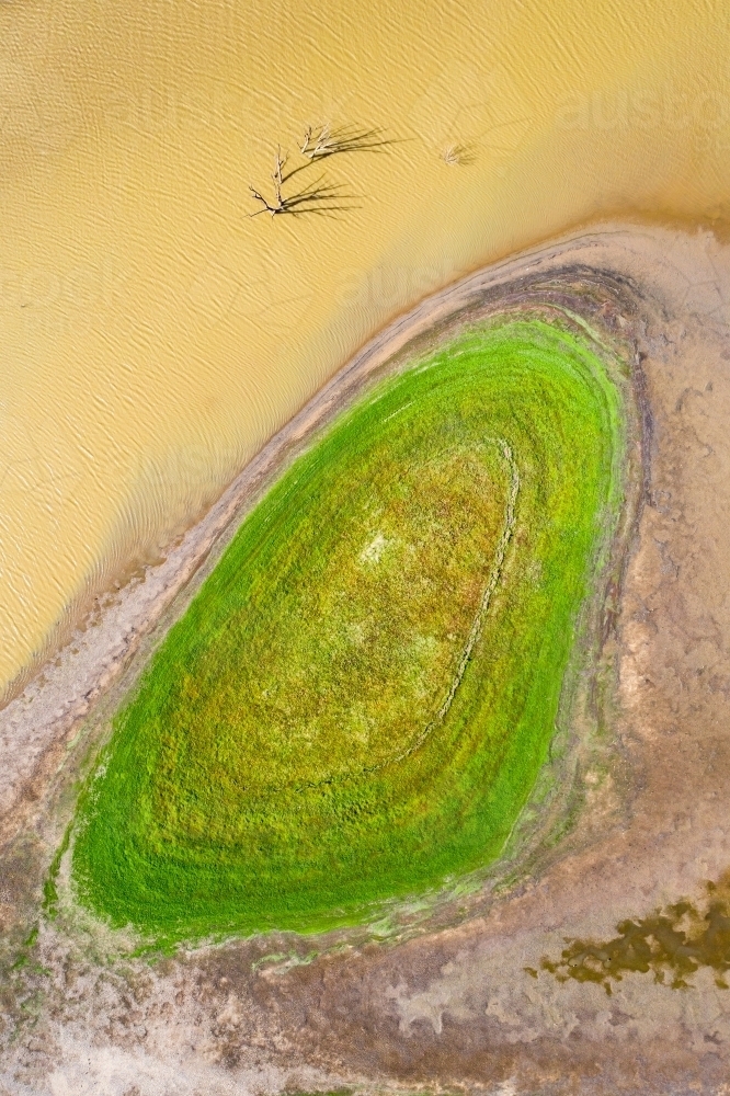 Looking down on patch of green land next to a muddy river - Australian Stock Image