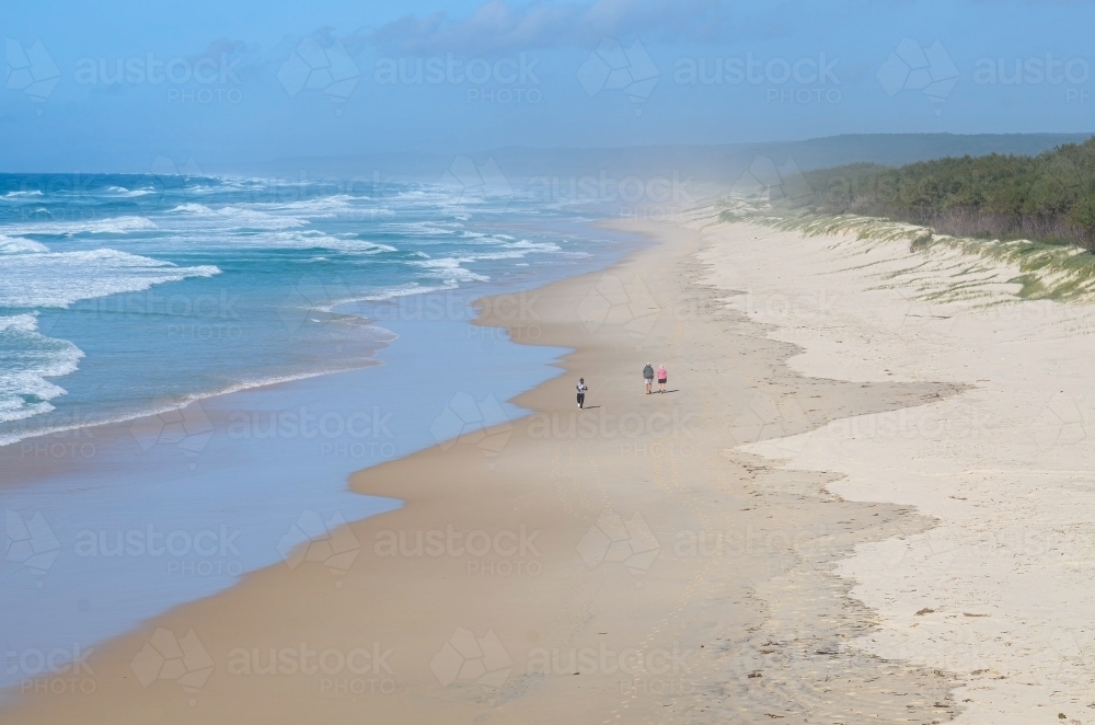 Looking down on people walking in the distance on a long ocean beach - Australian Stock Image