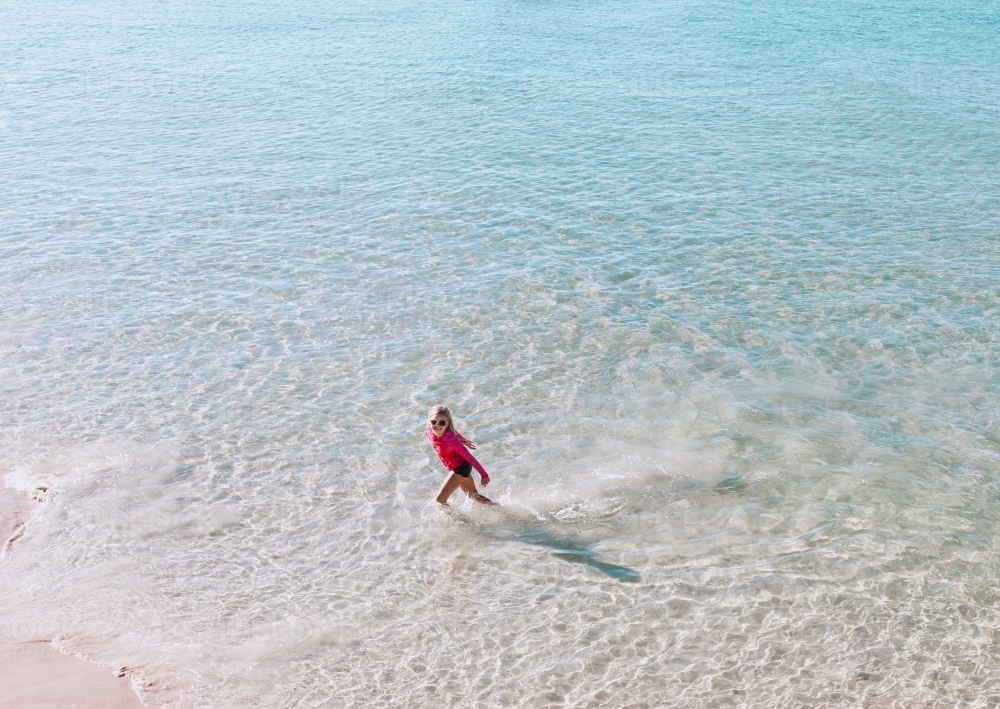 Looking down on young girl walking through crystal clear waters at beach - Australian Stock Image
