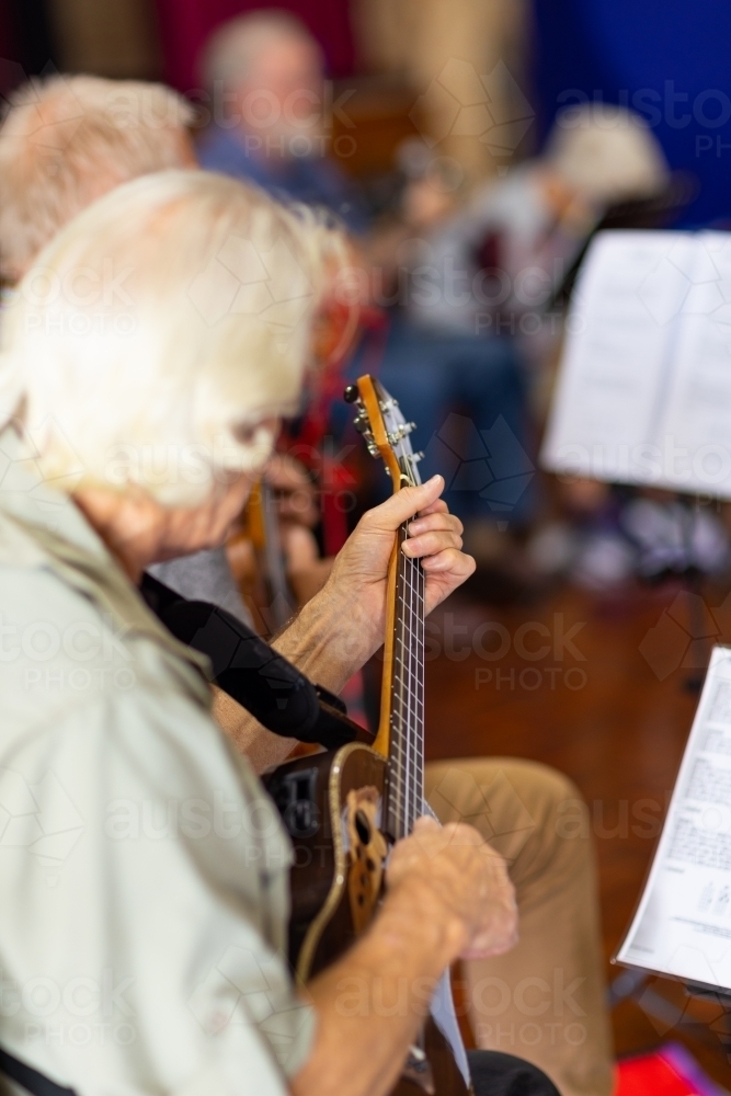 looking down over the shoulder of a guy playing ukulele in a group - Australian Stock Image