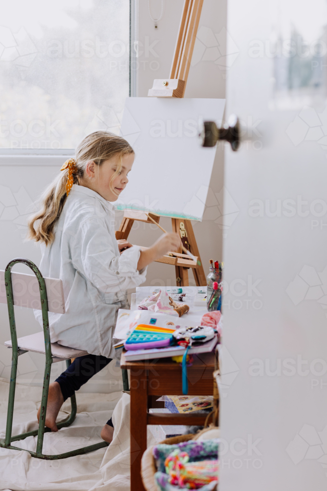 Looking into a room where Girl painting on canvas at home studio - Australian Stock Image