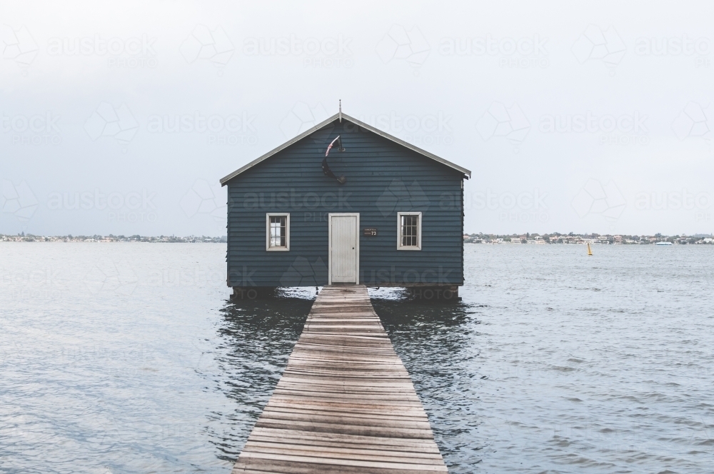 Looking out along a pier to a blue boat shed on a river - Australian Stock Image