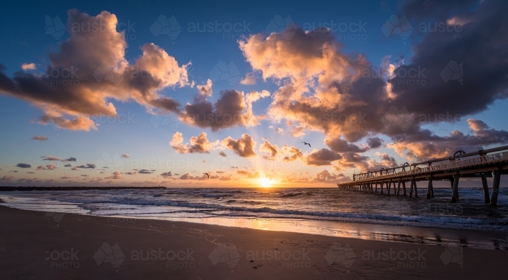 Looking out at sunrise from a beach with pier - Australian Stock Image
