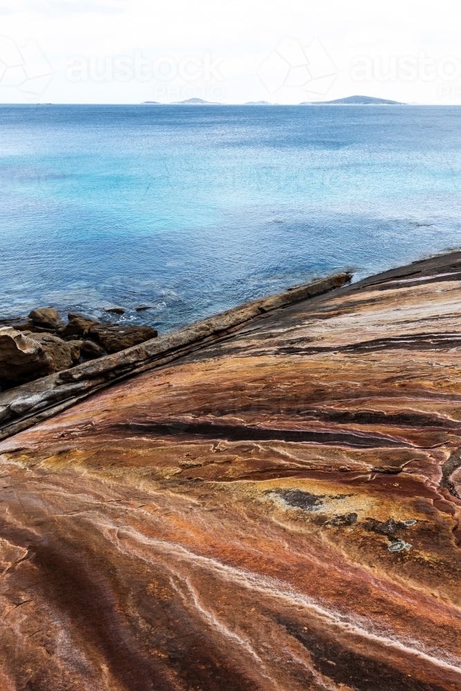 Looking out over patterned, textured, colourful rock face toward the ocean - Australian Stock Image