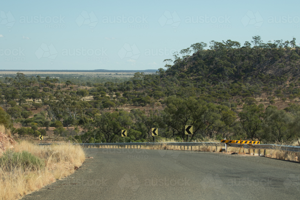 Looking over a bend in the bitumen road to the outback landscape beyond - Australian Stock Image