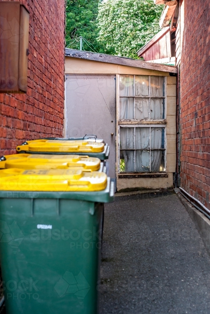 Looking past some wheelie bins to a small cottage garden entrance - Australian Stock Image