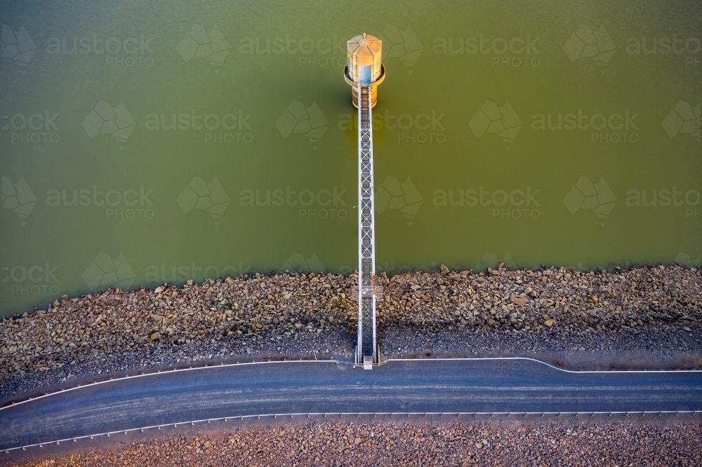 Looking straight down on a water tower connected to a dam wall by a steel walkway - Australian Stock Image