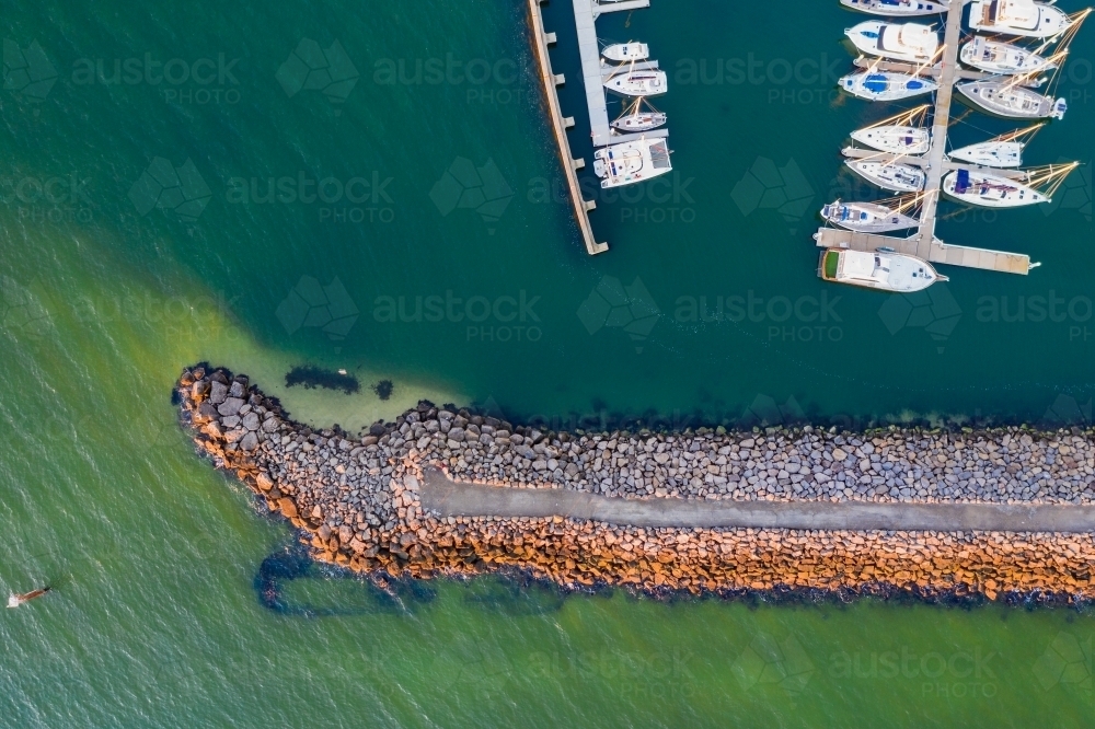 Looking straight down on the end of a narrow rock breakwater shielding rows of yachts - Australian Stock Image
