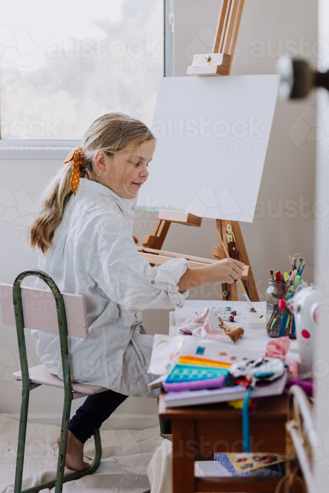 Looking through a door into a home studio where girl is painting on canvas - Australian Stock Image