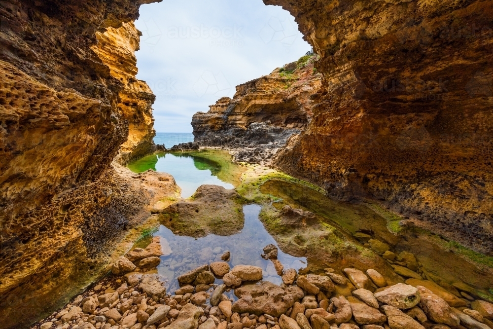 Looking through a jagged rock formation over still rock pools - Australian Stock Image