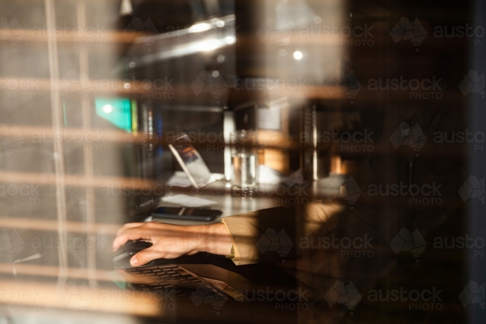 Looking through window at person in home office using computer mouse - Australian Stock Image