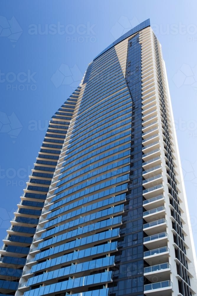 Looking up at a single tall high rise building against blue sky - Australian Stock Image