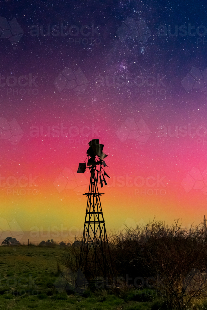 Looking up at a starry night above colourful Aurora Australis over a silhouetted windmill - Australian Stock Image