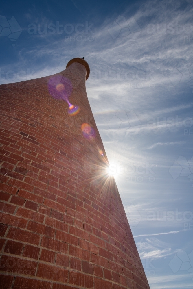 looking up at an old brick lighthouse with a sun flare, and blue sky - Australian Stock Image