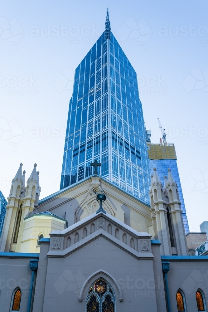 Looking up at an old church facade in front of a modern glass skyscraper. - Australian Stock Image