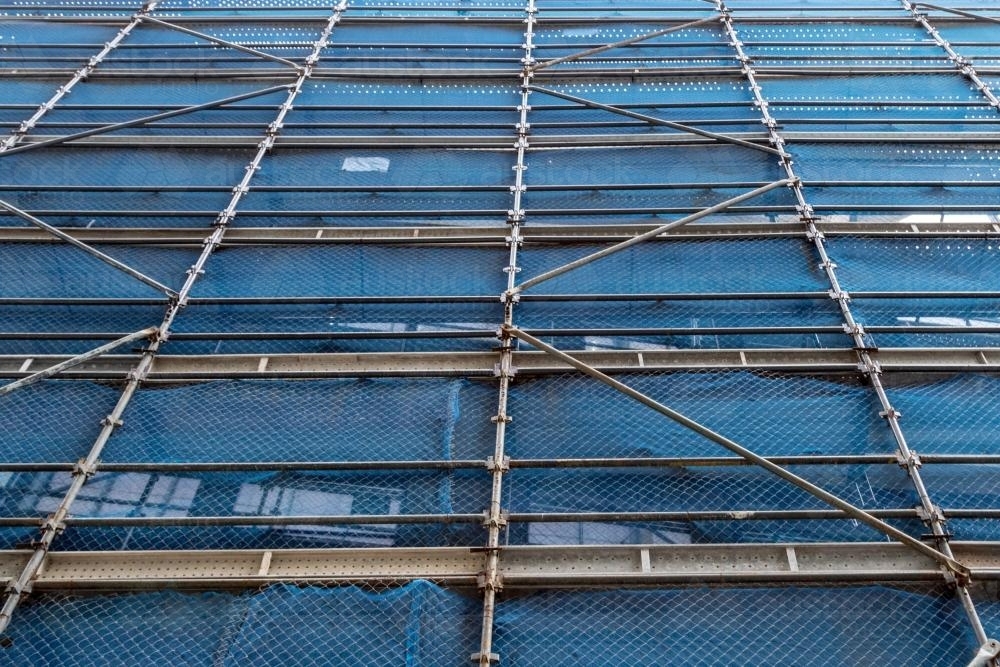 Looking up at city building covered in scaffolding and blue - Australian Stock Image