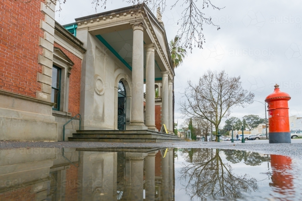 Looking up at the facade of an historic building and mailbox reflected in a puddle - Australian Stock Image