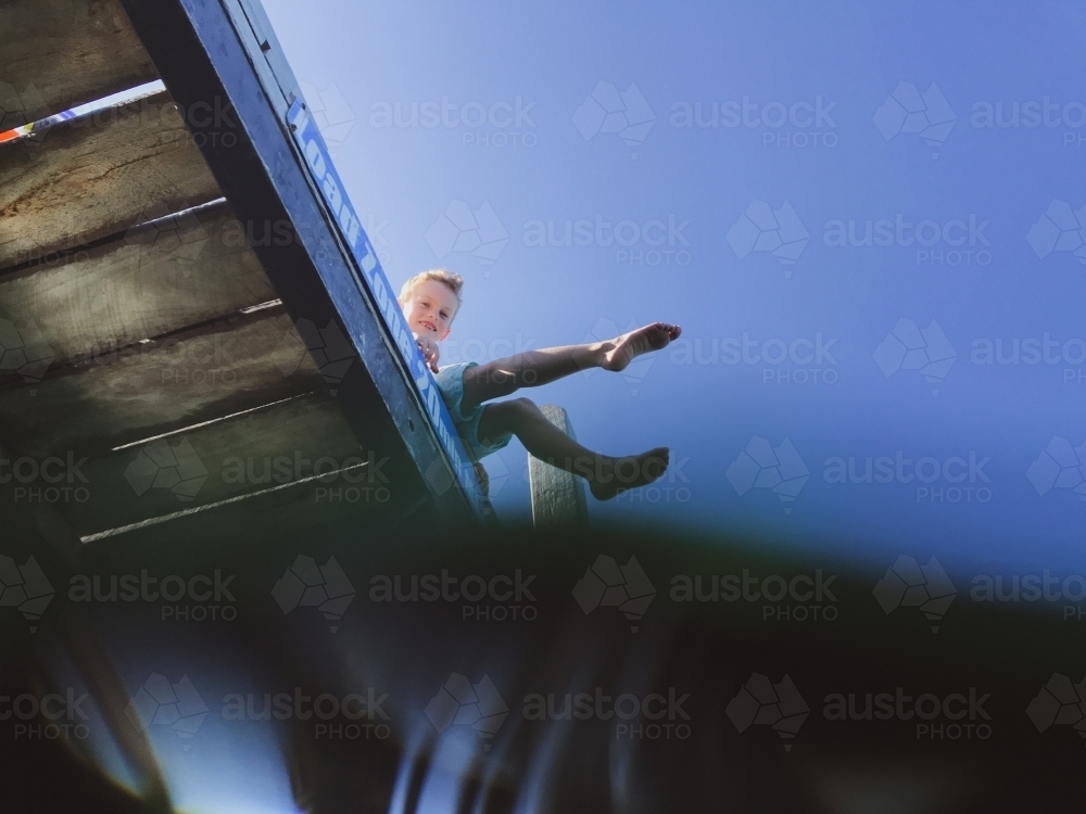 Looking up from the water at boy sitting on jetty - Australian Stock Image