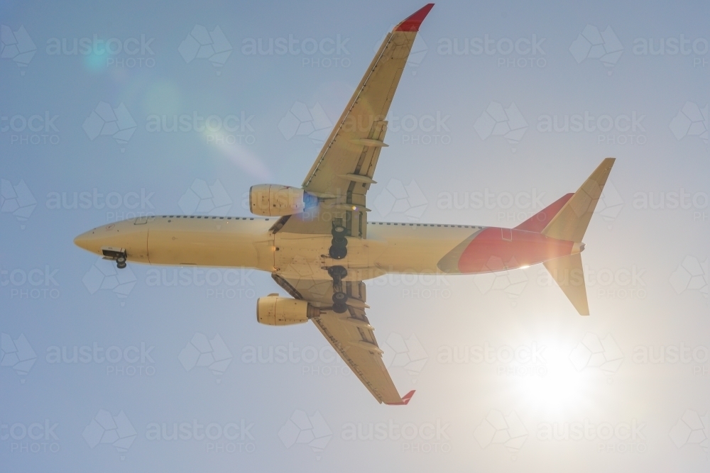 Looking up underneath a large jet as in flies past the Sun in a blue sky - Australian Stock Image