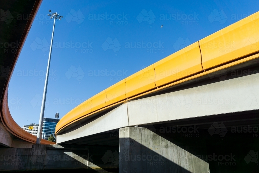 Looking up underneath curved freeway on ramps and a single light pole against a blue sky - Australian Stock Image