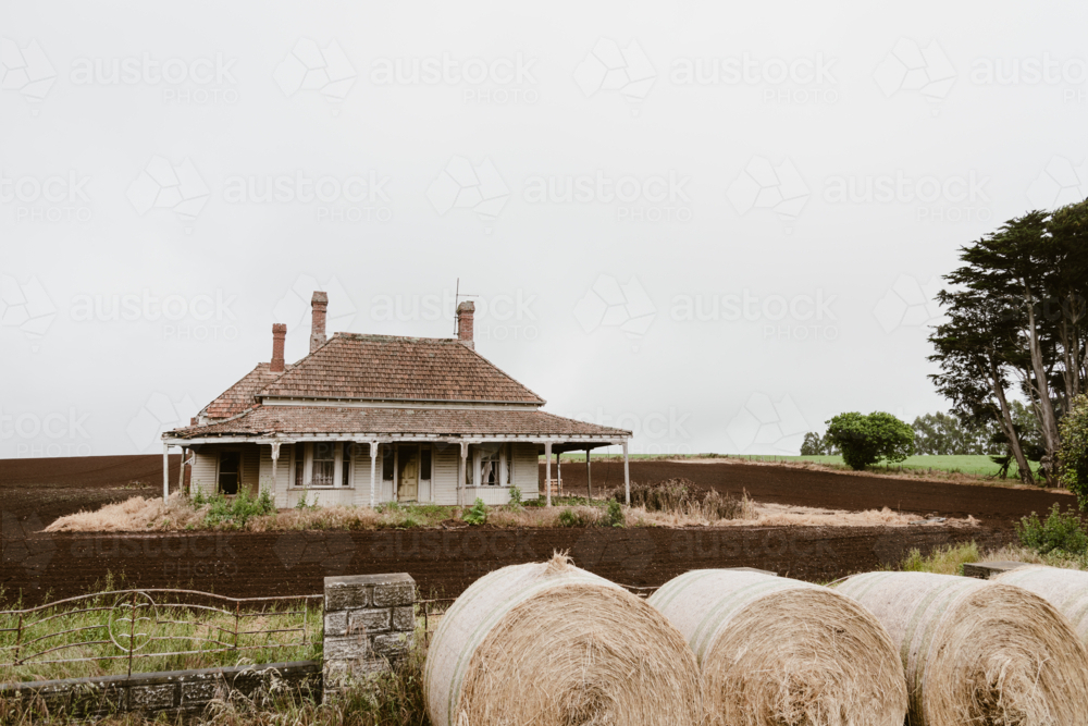 lovely old farm house in the middle of a farmed field with round hay bales along the front fence - Australian Stock Image