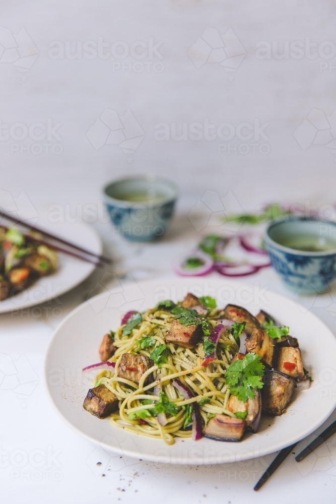 Low angle of cold soba noodle, eggplant and parsley salad with green tea on white background - Australian Stock Image