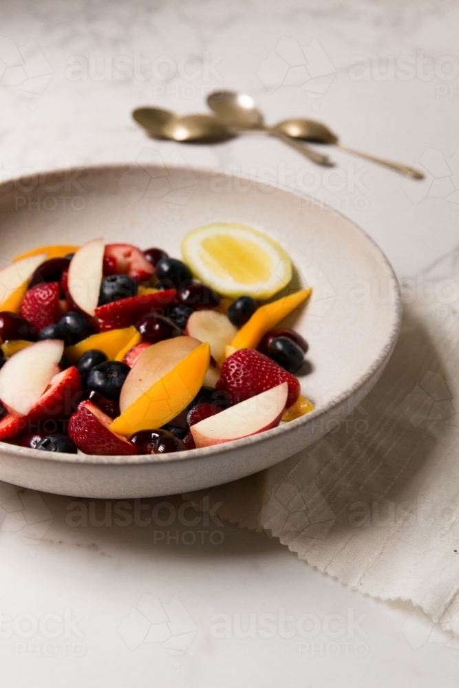 Low angle of styled, naturally lit and colourful mixed berry and stone fruit salad on marble table - Australian Stock Image