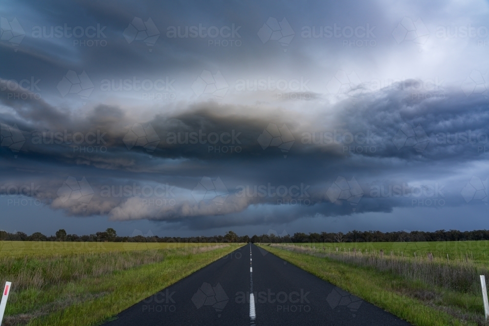Low angle view of a country road running under a dark dramatic stormfront - Australian Stock Image
