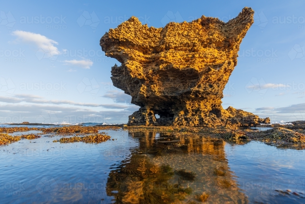 Low angle view of a craggy rock formations sticking out of  rock pools in late afternoon sunshine - Australian Stock Image
