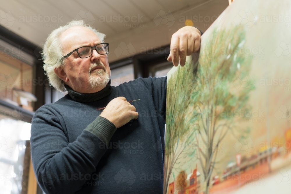 Low angle view of a distinguished male artist leaning on a painted canvas - Australian Stock Image