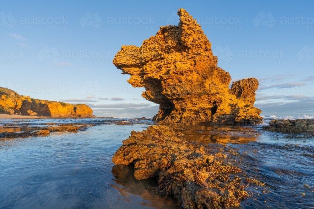 Low angle view of a sandstone rock formations sticking out of  rock pools in late afternoon sunshine - Australian Stock Image