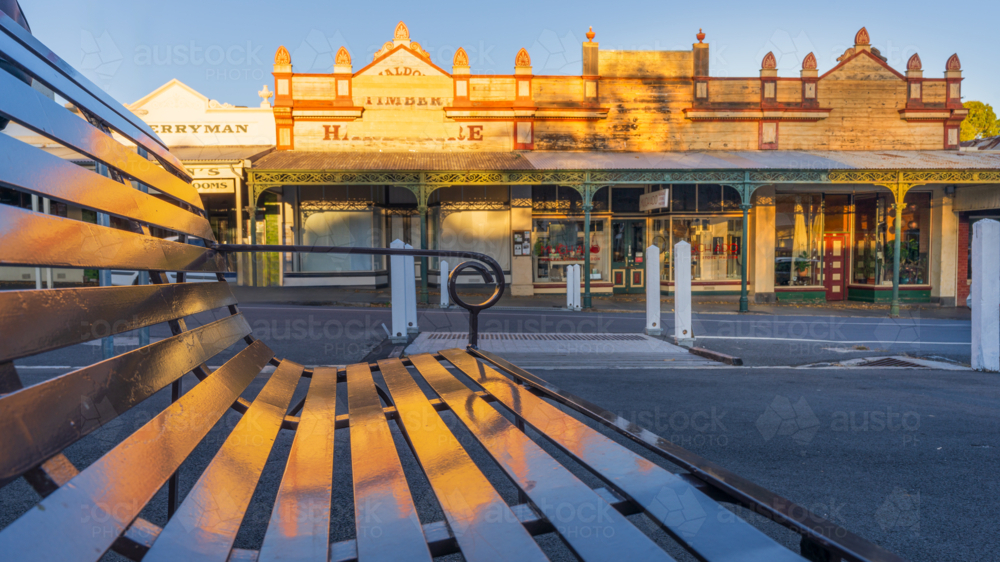 Low angle view of a street bench reflecting an historic building facade bathed in golden light - Australian Stock Image