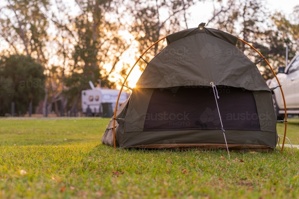 Low angle view on a sleeping swag set up on a grassy area of a campground at sunset - Australian Stock Image