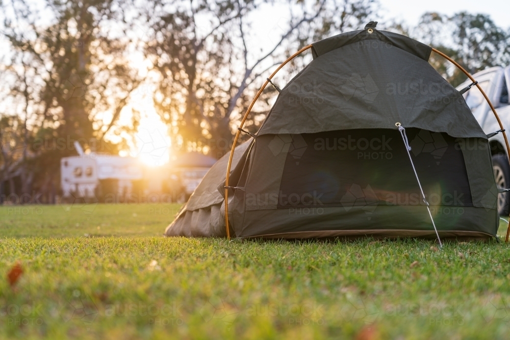 Low angle view on a sleeping swag set up on a grassy area of a campground at sunset - Australian Stock Image