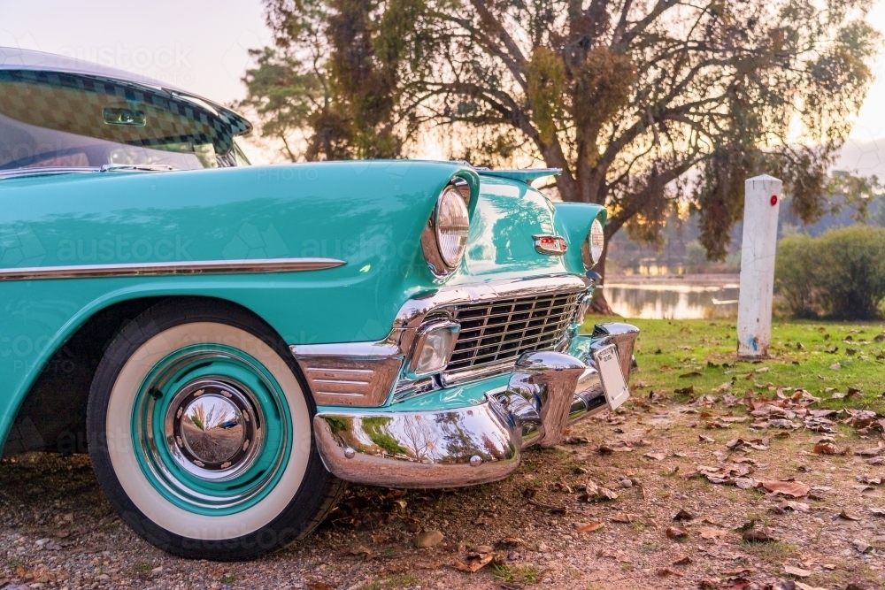 Low angled view of a brightly coloured classic car parked on a leafy dirt road under a tree - Australian Stock Image